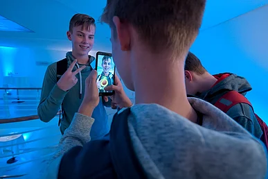 Ein junger Mann nimmt einen anderen mit dem handy auf, auf dem Bildschirm ist das Bild bearbeitet