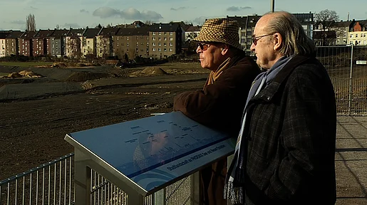 Zwei ältere Männer gucken auf die Brache, die bald geflutet werden soll. 