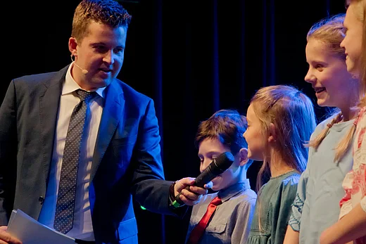 Moderator Tim Gailus interviewt die Kinderjury, er h&auml;lt einem M&auml;dchen das Mikrofon vor den Mund