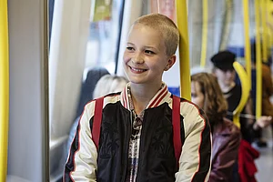 Ein M&auml;dchen steht lachend in einer Stra&szlig;enbahn. 