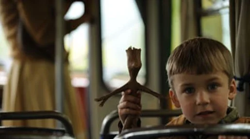 Szenenbild: Der Junge schaut über die Lehne eines Sitzes