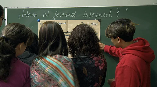 Szenenbild: Schüler und Schülerinnen stehen vor einer Tafel