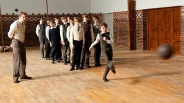 Szenenbild: Die Jungen stehen in einer Reihe. Einer von ihnen hüpft vor dem Lehrer