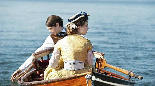 Szenenbild: ein junges Paar in historischen Kostümen in einem Ruderboot auf einem See