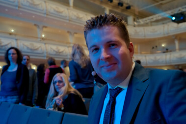 Porträtaufnahme von Moderator Tim Gailus, im Hintergrund Festsaal des Kaisersaals