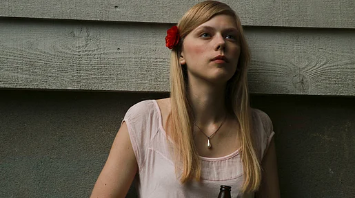 Szenbild: Alma vor einer Wand mit einer Bierflasche in der Hand
