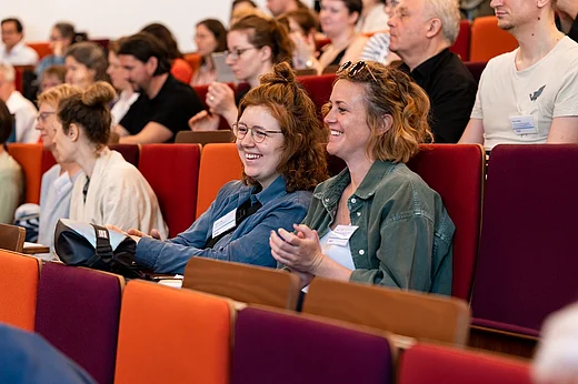 Gef&uuml;llte Sitzreihen, im Bildmittelpunkt zwei lachende Frauen