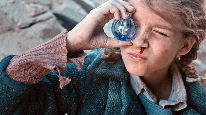 Szenenbild: Christl schaut durch eine gro&szlig;e Glasmurmel, im Hintergrund Tr&uuml;mmer