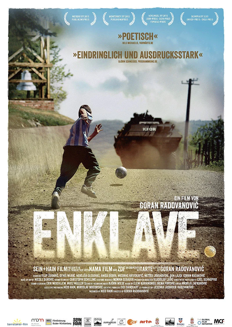 Ein junge rennt einem Ball hinterher, im Hintergrund sieht man einen Panzer. 