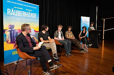 F&uuml;nf Personen auf der B&uuml;hne vor Aufsteller mit Werbung f&uuml;r den Film R&Auml;UBERH&Auml;NDE