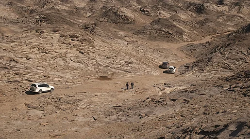 Drei Autos auf dem Weg durch eine bergige Wüstenlandschaft.