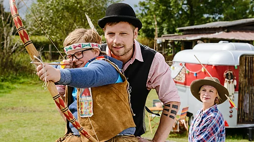 Szenenbild: Winnetous Sohn in voller Montur und sein Vater üben Bogenschießen