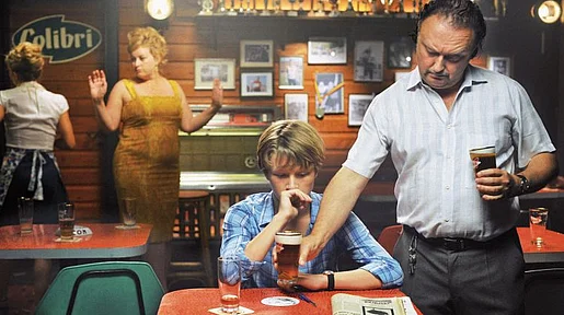 Szenenbild: In einer Kneipe: Einem sehr jungen Mann wird von einem älteren ein Bier hingestellt