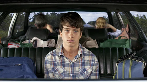 Szenenbild: Der Protagonist mit gelangweilten Blick im Fond eines Autos