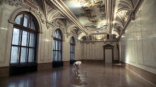 Szenenbild: Ein Mann in einem leeren Museums-Salon. Mit einem Hammer ist er am Boden beschäftigt