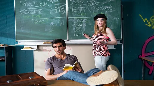 Szenenbild: Chantal an der Tafel, während der Aushilfslehrer mit den Füßen auf dem Pult in die Klasse schaut