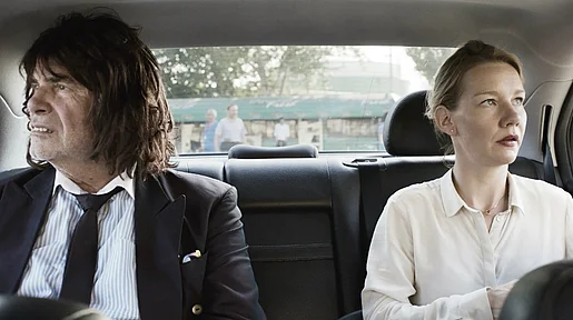 Szenenbild: Toni Erdmann und seine Tochter im Fond eines Autos, sie blicken in entgegengesetzte Richtungen aus dem Seitenfenster