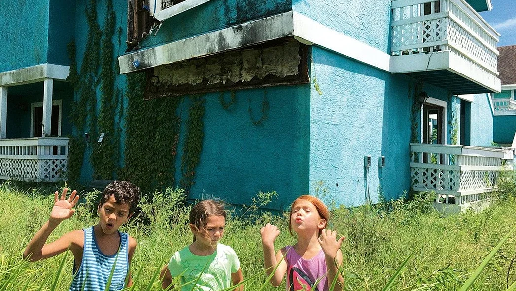 Drei Kinder in hohem Gras vor einem blauen Haus 