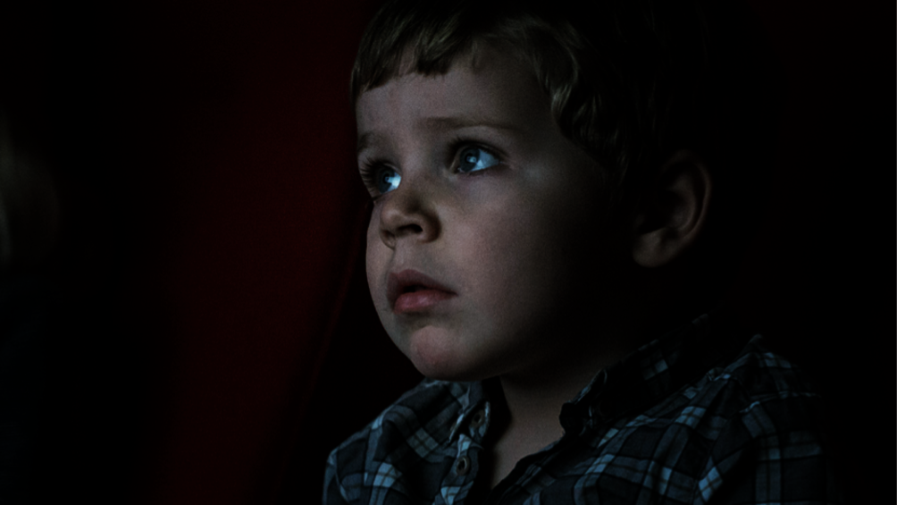 Gesicht eines kleinen Jungen in einem Kinosessel sitzt und gebannt auf die Leinwand schaut