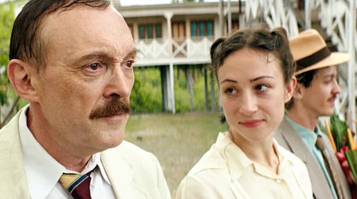 Szenenbild: Josef Hader als Stefan Zweig links im Bildvordergrund, dahinter seine Frau Lotte. Beide tragen weiße Kleidung, im Hintergrund Palmen, grün und ein weißes Haus sowie ein weiterer Mann mit Strohhut
