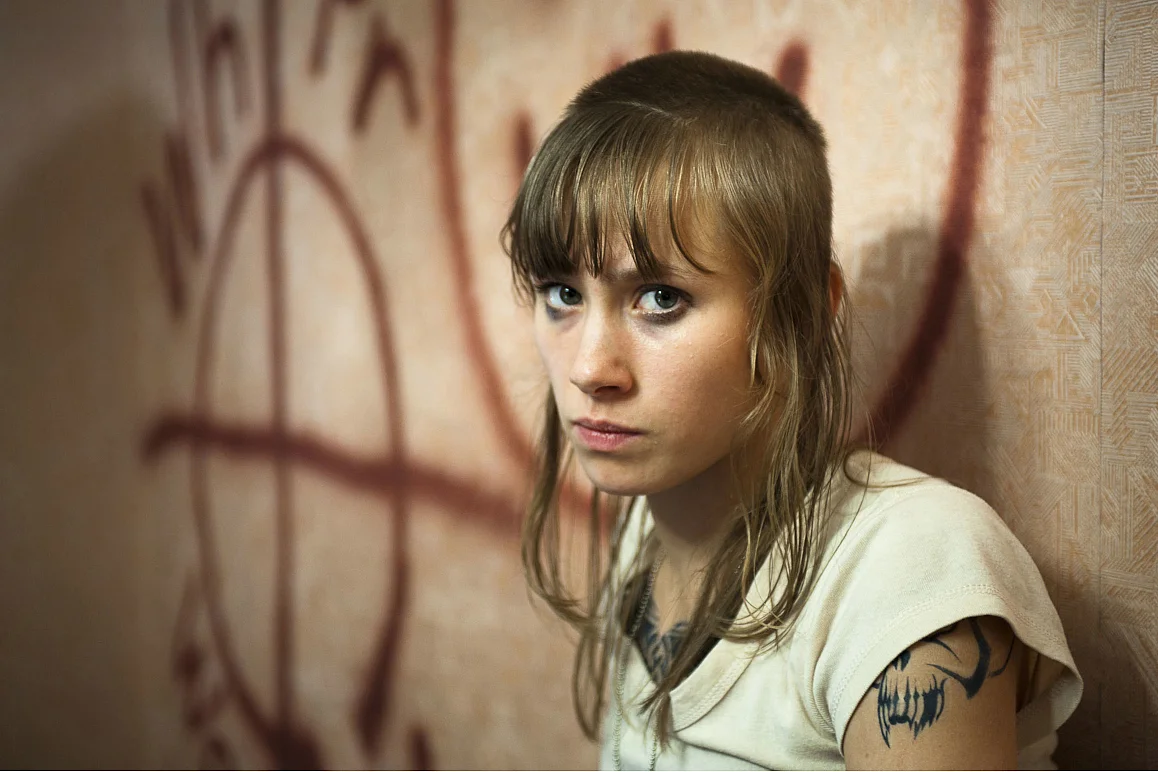 Eine junge Frau steht vor einer Wand mit Graffiti und schaut w&uuml;tend in die Kamera