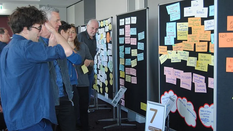 Personen betrachten Pinw&auml;nde mit bunten Zetteln, die Personen stehen in der linken Bildh&auml;lfte