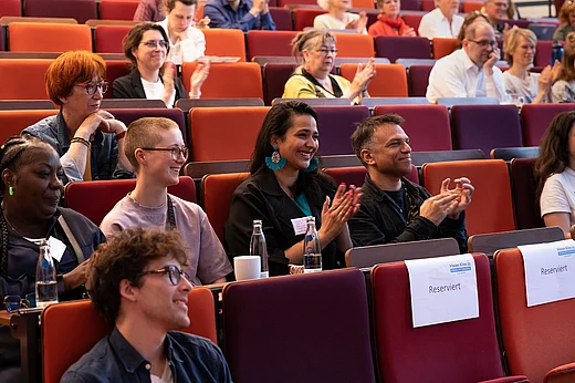 Lachende und applaudierende Menschen in H&ouml;rsaal-Sesselreihen