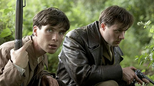 Szenenbild: Zwei Männer mit Waffen hocken im Gebüsch