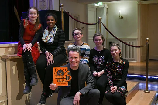 Preistr&auml;ger Hermans mit Kindertiger-Troph&auml;e, hinter sich auf einer Treppe sitzend die Mitglieder der Kinderjury