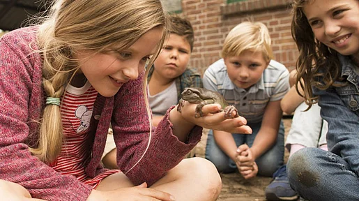 Szenenbild: Hauptprotagonistin Sita inmitten einer Kindergruppe, auf ihrer ausgestreckten Hand sitzt ein Frosch