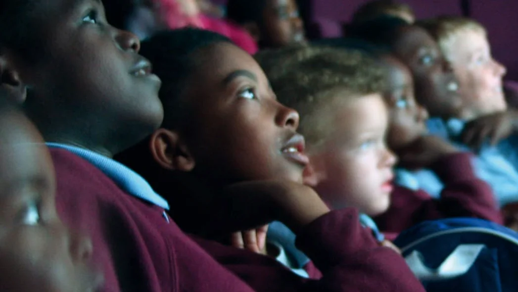 Kinder im Kino schauen gebannt Richtung Leinwand, das Licht spiegelt sich in ihren Gesichtern