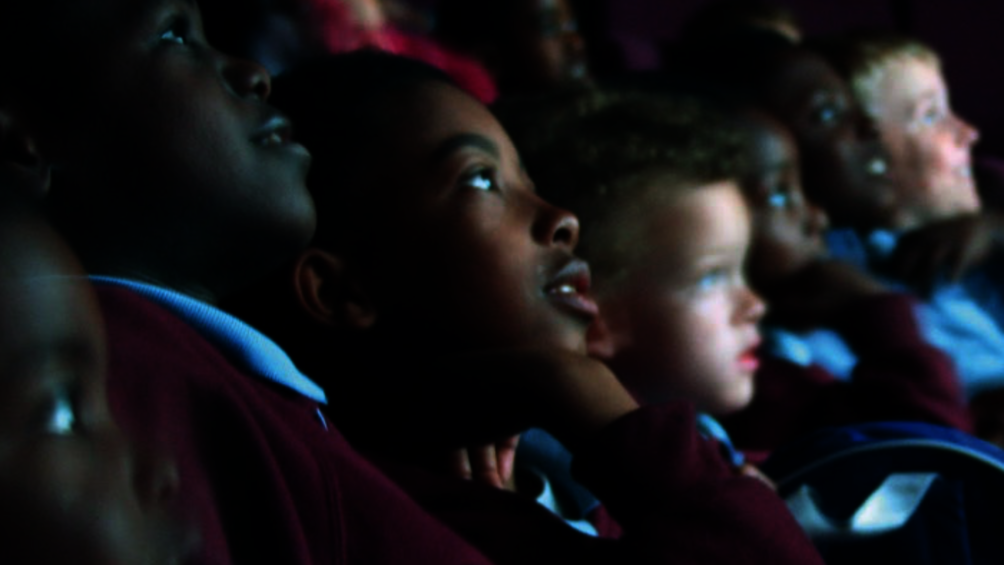 Kinder im Kino schauen gebannt Richtung Leinwand, das Licht spiegelt sich in ihren Gesichtern