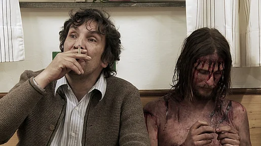 Szenenbild: Ein Mann mit Zigarette neben einem Jesusdarsteller