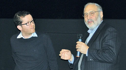 Szenenbild: Zwei Männder vor dunklem Hintergrund, einer mit Mikrofon in der Hand