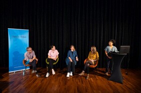Fünf Personen sitzend, eine stehend, auf der Bühne eines Kinos