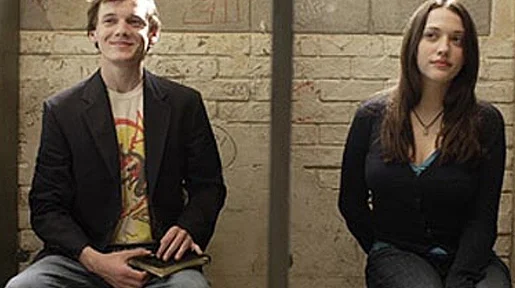 Szenenbild: Ein Junge und ein Mädchen sitzen vor einer Steinwand