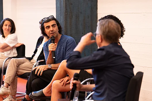 Regisseur Fatih Akin spricht in ein Mikrofon, er sitzt neben anderen Panelisten