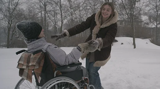 Szenenbild: Mateus, im Rollstuhl sitzend, und eine junge Pflegerin toben im Schnee