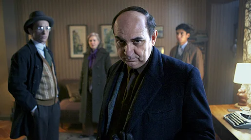 Szenenbild: Pablo Neruda im Vordergrund in einem etwas düsteren Raum, im Hintergrund weitere Personen