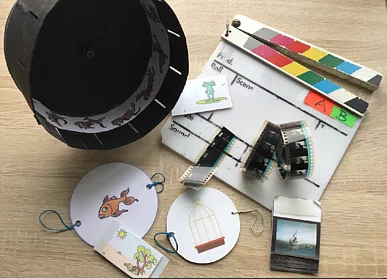Verschiedene optische Spielzeuge, eine Filmklappe und eine Filmrolle liegen auf einem Tisch 