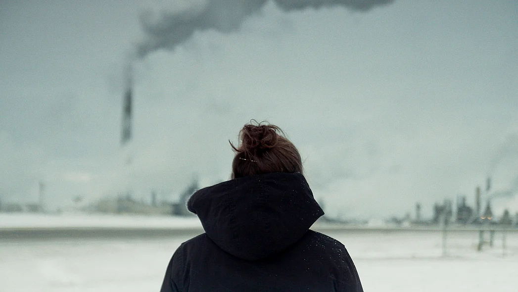 Eine Frau mit Dutt ist von hinten zu sehen. Sie schaut auf eine weite Industrielandschaft.