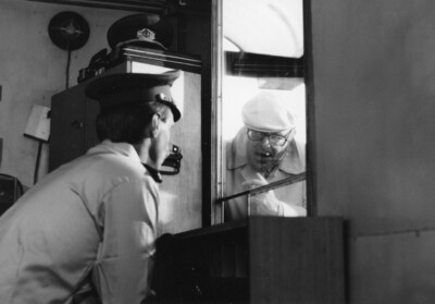 Marcel Ophüls guckt durch ein Fenster in ein Grenzhäuschen, um ein Interview mit einem Grenzer zu führen.