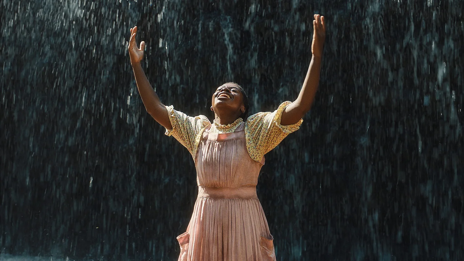 Standbild aus dem Film, Celia steht mit erhobenen Armen und zur&uuml;ckgelegtem Kopf, im Hintergrund Tropfen eines Wasserfalls