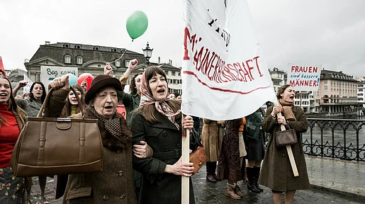 Szenenbild:Demonstrationszug von Frauen mit Transparenten, im Vordergrund Nora
