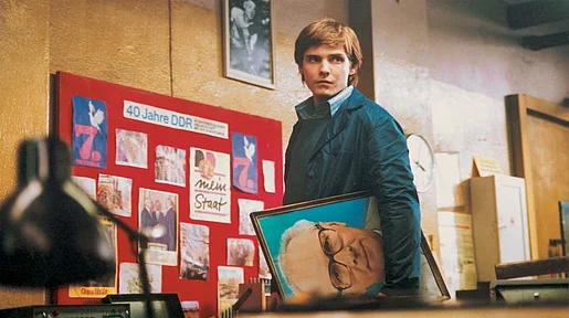Alex steht mit einem Porträit von Erich Honecker in der Hand vor einem Schaubild zum Thema 40 Jahre DDR.