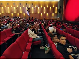 Eine Gruppe Sch&uuml;ler:innen sitzt in einem gef&uuml;llten Kinosaal und l&auml;chelt in die Kamera