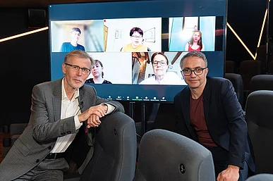 V&ouml;lkert und Gr&uuml;n vor einem Bildschirm mit den Beteiligten des Werkstattgespr&auml;chs