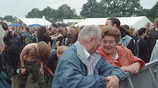 Szenenbild: An der Bühne: ein altes Ehepaar, im Hintergrund Heavy matal Fans
