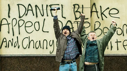 Szenenbild: Daniel Blake und ein Passant reißen die Arme in die Höhe vor der Wand, die Daniel mit einer Parole besprüht hat