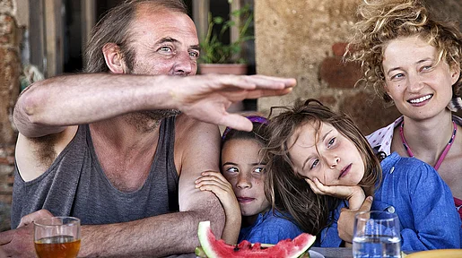 Die Familie sitzt an einem Tisch redet und isst Wassermelone.